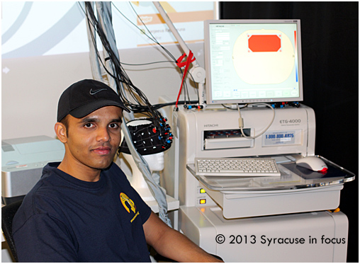 Danushka Bandara sits at the fNIRS device, which measures blood flow in the brain.